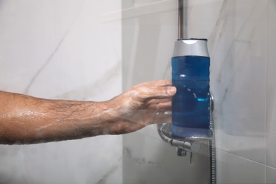 Man taking bottle of gel from shelf in shower at home, closeup