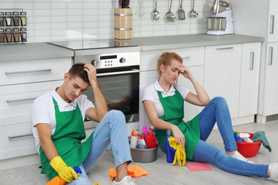 Exhausted janitors sitting on floor in kitchen. Cleaning service