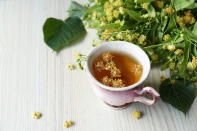 Photo of Cup of aromatic tea with linden blossoms on white wooden table, space for text