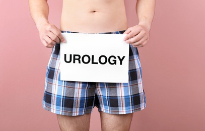 Young man holding paper with word UROLOGY on color background