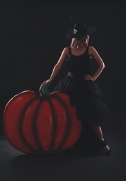 Young woman wearing witch costume near decorative pumpkin on black background. Halloween party