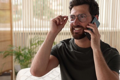 Handsome man talking on smartphone at home, space for text