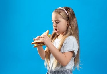 Photo of Cute little girl eating tasty sandwich on light blue background