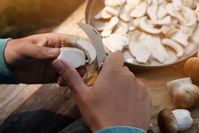 Man cutting mushroom with knife at wooden table, closeup