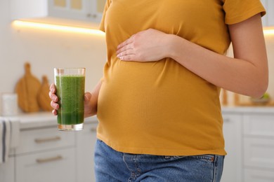 Young pregnant woman with smoothie in kitchen, closeup. Healthy eating