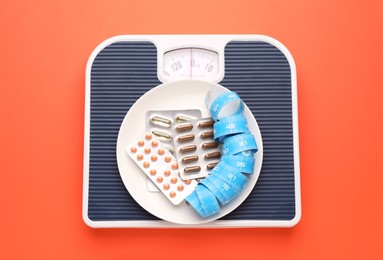 Scales with plate, weight loss pills and measuring tape on coral background, top view