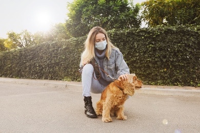 Woman in protective mask with English Cocker Spaniel outdoors. Walking dog during COVID-19 pandemic