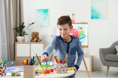 Little child painting picture at table indoors