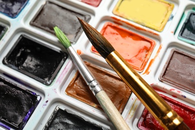 Plastic palette with colorful paints and brushes, closeup