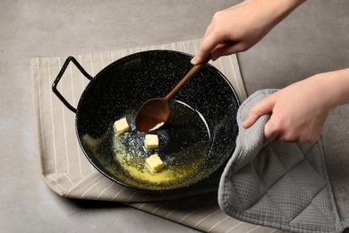 Photo of Woman mixing melting butter in frying pan on table, closeup