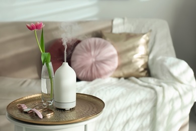 Photo of Aroma oil diffuser, tulip in vase and accessories on table indoors. Space for text