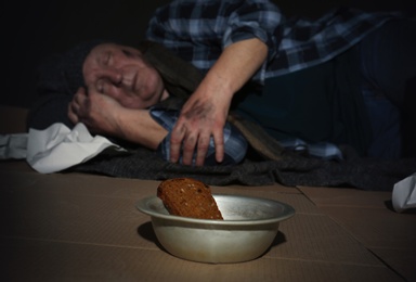 Bowl with bread and poor senior man on floor