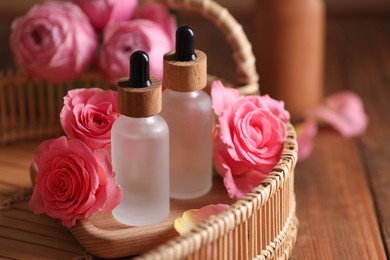 Tray with bottles of essential rose oil and flowers on wooden table, closeup