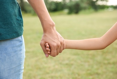 Woman holding hands with her child outdoors, closeup. Happy family