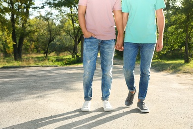 Gay couple with wristbands holding hands outdoors. Space for text