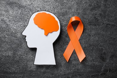 Human head cutout, brain and orange ribbon on grey table, flat lay. Multiple sclerosis concept