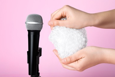 Woman making ASMR sounds with microphone and bubble wrap on pink background, closeup