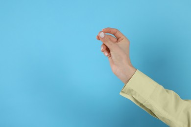 Woman snapping fingers on light blue background, closeup of hand. Space for text