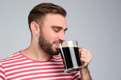 Handsome man with cold kvass on light grey background. Traditional Russian summer drink