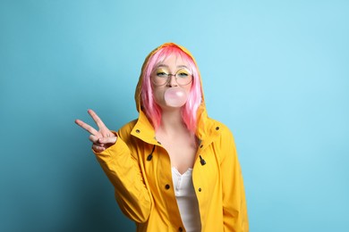 Photo of Fashionable young woman in pink wig with bright makeup blowing bubblegum on yellow background