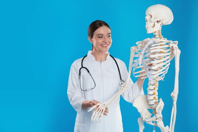Female orthopedist with human skeleton model on blue background