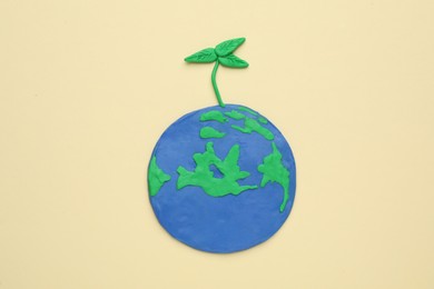 Plasticine model of planet with green seedling on beige background, top view. Earth Day