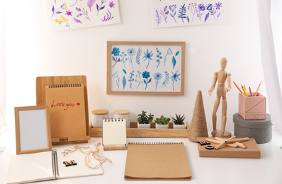 Wooden human figure and stationery on white table indoors. Interior elements