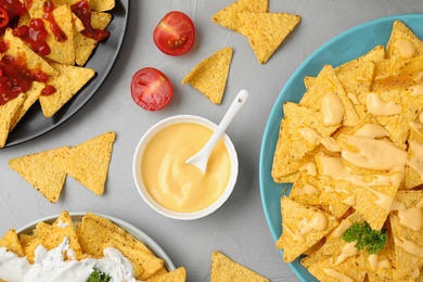 Mexican nacho chips with different sauces on grey table, flat lay