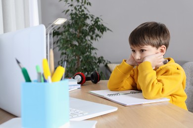 Cute little boy with modern laptop studying online at home. E-learning