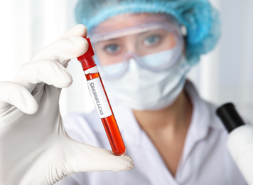Scientist holding test tube with blood sample and label CORONA VIRUS in laboratory, focus on hand