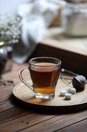 Photo of Tray with cup of freshly brewed tea and sugar cubes on wooden table indoors