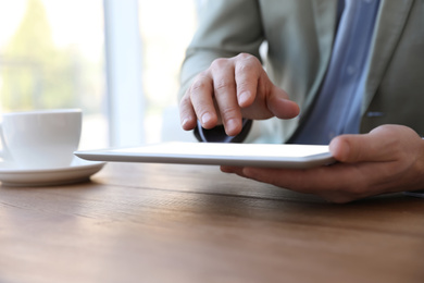 Businessman working with modern tablet at wooden table in office, closeup