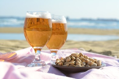 Photo of Glasses of cold beer and pistachios on sandy beach near sea, closeup