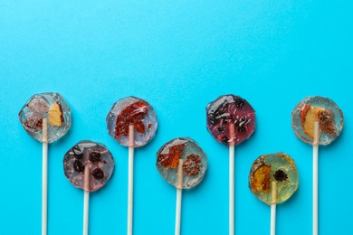 Sweet colorful lollipops with berries on light blue background, flat lay