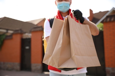 Courier in protective mask and gloves with order outdoors, closeup. Restaurant delivery service during coronavirus quarantine