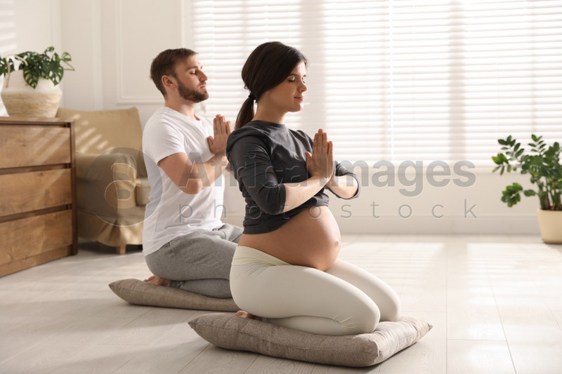 Young pregnant woman with her husband practicing yoga at home