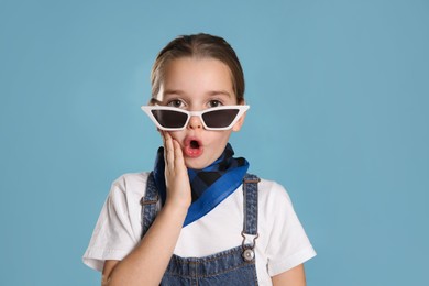 Surprised little girl wearing stylish bandana and sunglasses on turquoise background