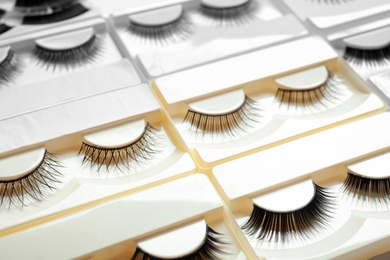 Set with different false eyelashes in packs as background, closeup