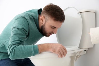 Young man suffering from nausea over toilet bowl indoors