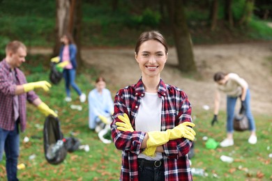 Photo of Young woman in gloves and group of people collecting garbage outdoors