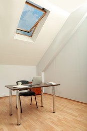 Photo of Stylish workplace with laptop and documents in attic room. Interior design
