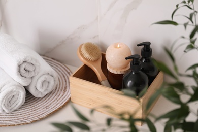 Wooden box with different toiletries, burning candle and clean towels on countertop in bathroom