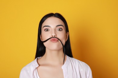 Photo of Funny woman making fake mustache with her hair on yellow background