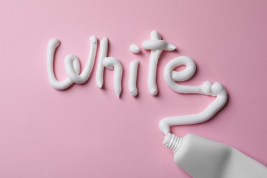 Word White written with toothpaste and tube on pink background, top view