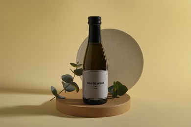 Bottle of delicious white wine and eucalyptus branches on beige background