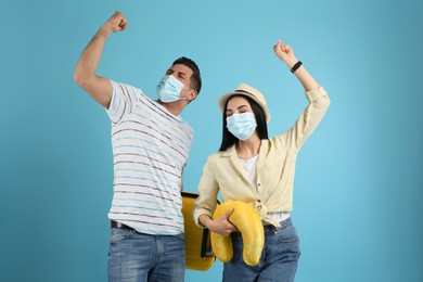 Couple of tourists in medical masks on light blue background. Travelling during coronavirus pandemic