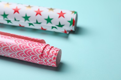 Different colorful wrapping paper rolls on turquoise background, closeup. Space for text