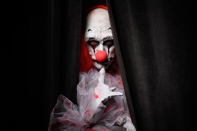 Terrifying clown hiding behind black curtains. Halloween party costume