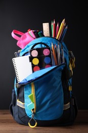 Backpack with different school stationery on wooden table near blackboard