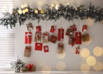 Christmas Advent calendar with gifts and decor hanging on white wall in room. Bokeh effect